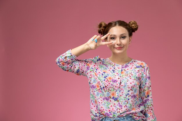 Vue de face jeune femme en chemise conçue de fleurs et jeans bleus souriant avec une expression mignonne sur le fond rose