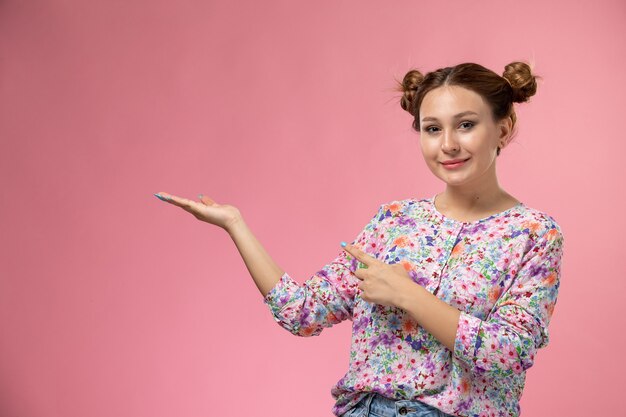 Vue de face jeune femme en chemise conçue de fleurs et jeans bleus souriant et posant sur fond clair