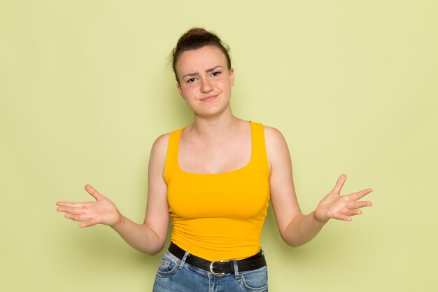 Une vue de face jeune femme en chemise jaune et jean bleu avec une expression mécontente