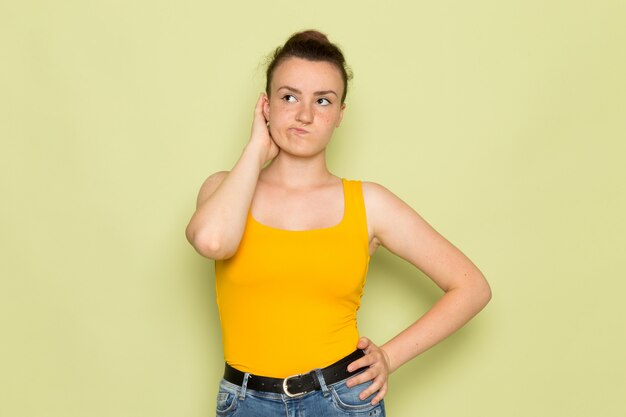 Une vue de face jeune femme en chemise jaune et jean bleu avec expression de la pensée