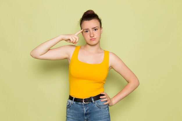 Une vue de face jeune femme en chemise jaune et jean bleu avec expression de la pensée