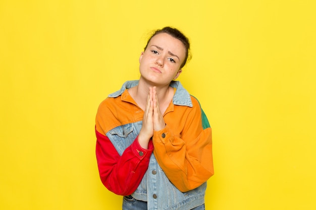 Une vue de face jeune femme en chemise jaune veste colorée et blue-jeans posant et priant