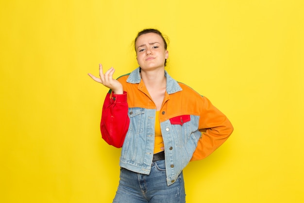 Une vue de face jeune femme en chemise jaune veste colorée et jeans bleu posant