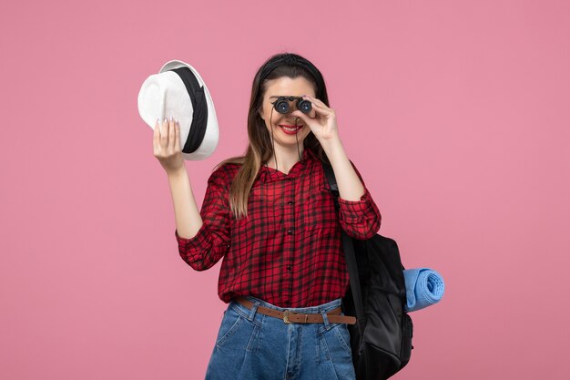 Vue de face jeune femme en chemise rouge à l'aide de jumelles sur le fond rose couleur femme humaine