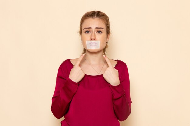 Vue de face jeune femme en chemise rouge avec bouche attachée sur l'espace crème émotion photo violence domestique