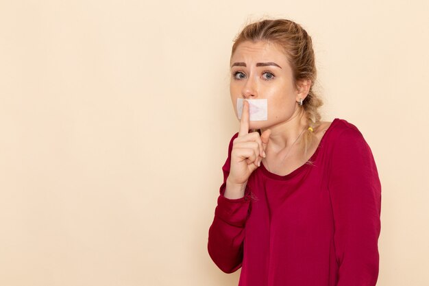 Vue de face jeune femme en chemise rouge avec bouche attachée montrant signe de silence sur le tissu femme espace crème