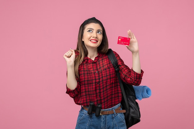 Vue de face jeune femme en chemise rouge avec carte bancaire sur le bureau rose femme couleur humaine