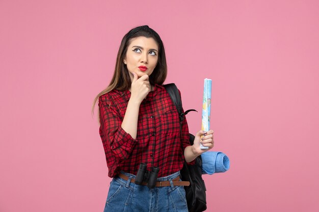 Vue de face jeune femme en chemise rouge avec carte sur fond rose clair mode femme