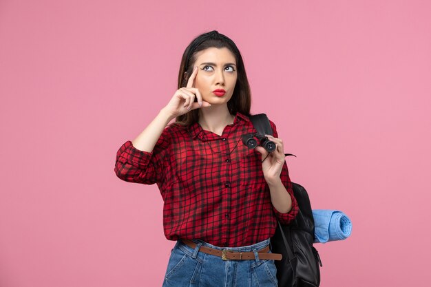 Vue de face jeune femme en chemise rouge avec des jumelles sur fond rose femme couleurs étudiant