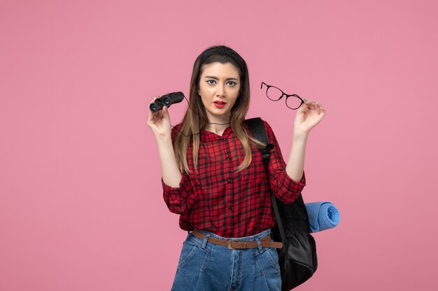 Vue de face jeune femme en chemise rouge avec des jumelles sur le modèle photo femme fond rose