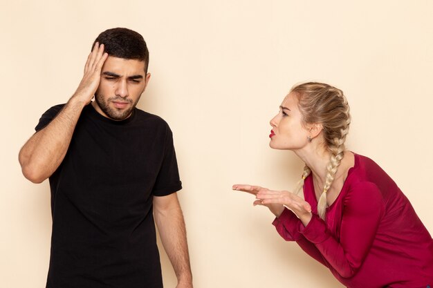 Vue de face jeune femme en chemise rouge quarelling avec homme sur l'espace crème femme tissu photo violence