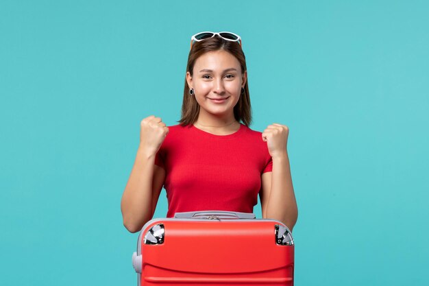 Vue de face jeune femme en chemise rouge avec sac rouge se prépare pour les vacances sur le bureau bleu