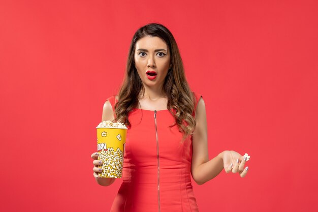 Vue de face jeune femme en chemise rouge tenant du pop-corn sur la surface rouge