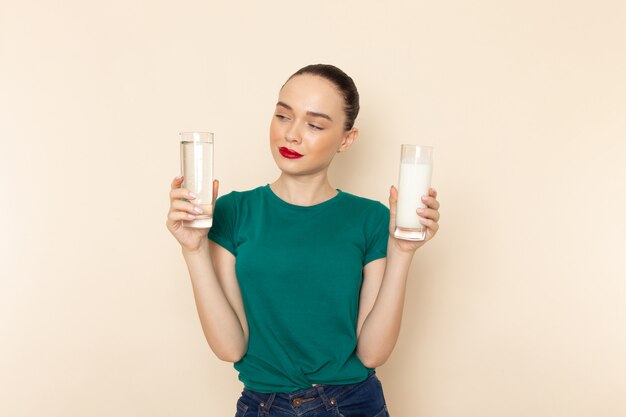 Vue de face jeune femme en chemise vert foncé et jean bleu tenant du lait et de l'eau sur beige