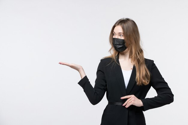 Vue de face d'une jeune femme choquée en costume portant un masque chirurgical et pointant quelque chose sur du blanc