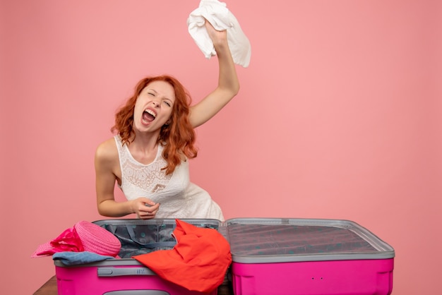 Vue de face de la jeune femme en colère jetant ses vêtements sur le mur rose