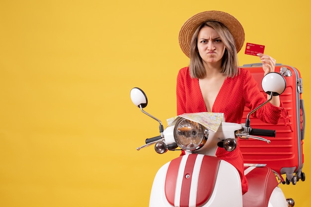 Photo gratuite vue de face de la jeune femme en colère en robe rouge tenant une carte de crédit près de cyclomoteur