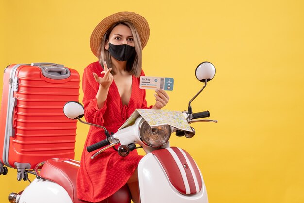 Vue de face de la jeune femme confuse avec un masque noir sur un billet de maintien de cyclomoteur