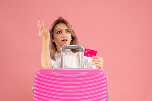 Vue de face de la jeune femme confuse tenant la carte derrière la valise