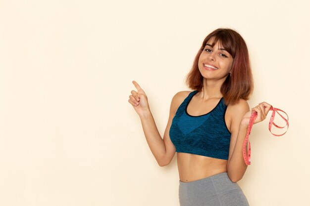 Vue de face de la jeune femme avec un corps en forme de chemise bleue avec sourire sur mur blanc clair