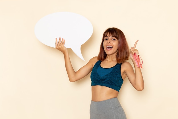 Vue de face de la jeune femme avec un corps en forme de chemise bleue tenant un énorme panneau blanc sur un mur blanc clair