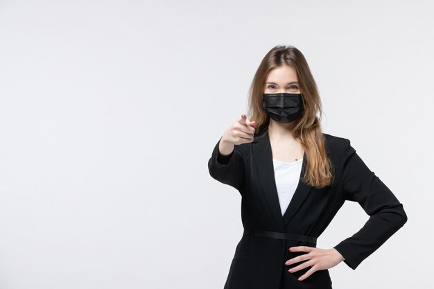 Vue de face d'une jeune femme en costume portant un masque chirurgical et pointant quelqu'un sur blanc