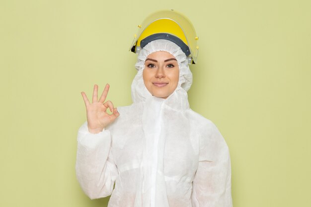 Vue de face jeune femme en costume spécial blanc et casque jaune souriant montrant bien signe sur l'emploi de l'espace vert