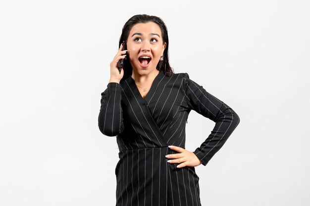 Vue de face jeune femme en costume strict sombre parlant au téléphone sur le fond blanc femme dame mode travailleur beauté emploi