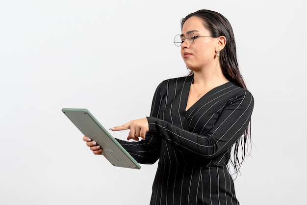 Vue de face jeune femme en costume strict sombre tenant une grosse calculatrice sur fond blanc travail femme dame mode travailleur beauté