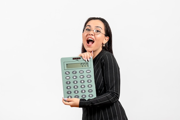 Vue de face jeune femme en costume strict sombre tenant une grosse calculatrice sur un travail de bureau blanc femme dame mode travailleur beauté