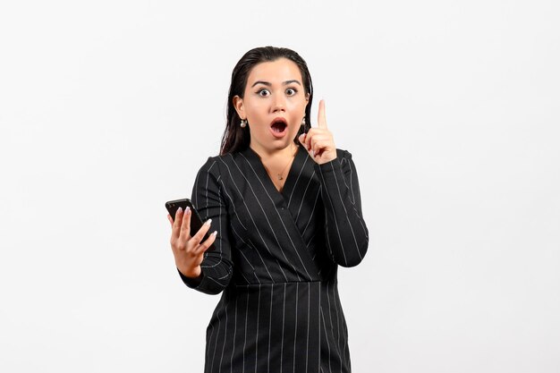 Vue de face jeune femme en costume strict sombre tenant un téléphone avec un visage choqué sur fond blanc femme dame mode employé de bureau beauté du travail