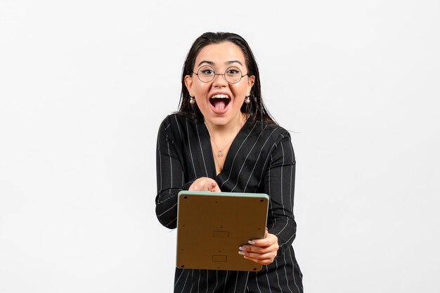 Vue de face jeune femme en costume strict sombre travaillant avec une énorme calculatrice sur un travail de bureau blanc femme dame beauté entreprise de mode