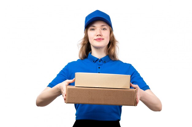 Une vue de face jeune femme courrier en chemise bleue casquette bleue et pantalon noir tenant des boîtes de livraison sur blanc