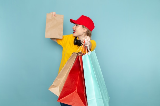 Vue de face jeune femme courrier en chemise jaune et cape rouge tenant multiplier et faire du shopping sur le travail de l'espace bleu