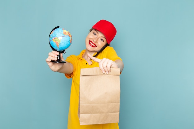 Vue de face jeune femme courrier en chemise jaune et cape rouge tenant le paquet globe parler au téléphone sur l'uniforme de l'emploi de l'espace bleu