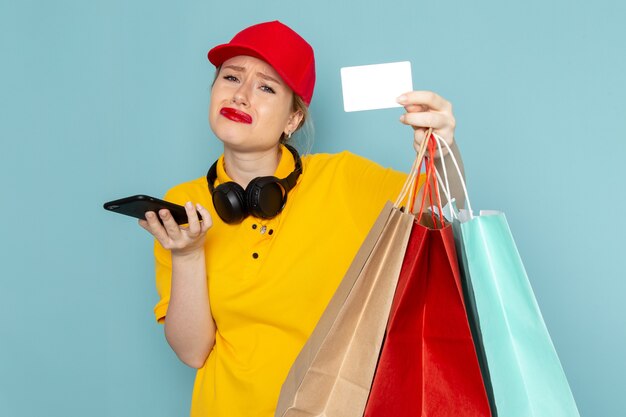 Vue de face jeune femme courrier en chemise jaune et cape rouge tenant des paquets commerciaux téléphone et carte sur l'espace bleu