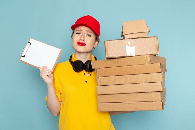 Vue de face jeune femme courrier en chemise jaune et cape rouge tenant plusieurs paquets et bloc-notes sur l'espace bleu