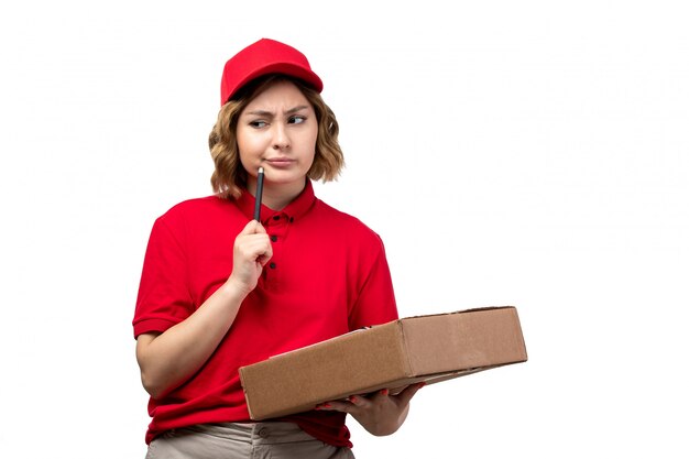 Une vue de face jeune femme courrier en chemise rouge bonnet rouge tenant des boîtes de livraison bloc-notes pensée