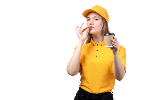 Une vue de face jeune femme courrier travailleur féminin du service de livraison de nourriture tenant une tasse de café et showign savoureux signe sur blanc