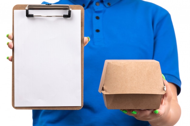 Photo gratuite une vue de face jeune femme courrier en uniforme bleu tenant le paquet de livraison de nourriture et le bloc-notes pour les signatures