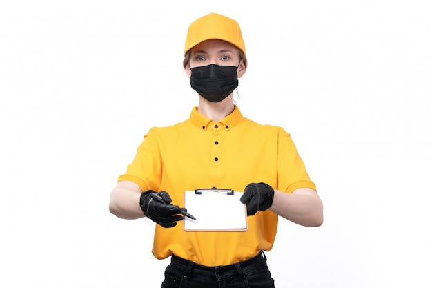 Une vue de face jeune femme courrier en uniforme jaune gants noirs et masque noir tenant le bloc-notes demandant la signature