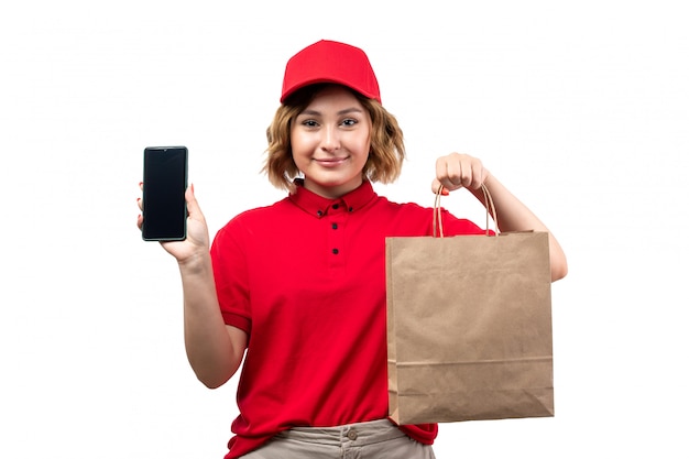 Une vue de face jeune femme courrier en uniforme tenant le colis de livraison et smartphone souriant