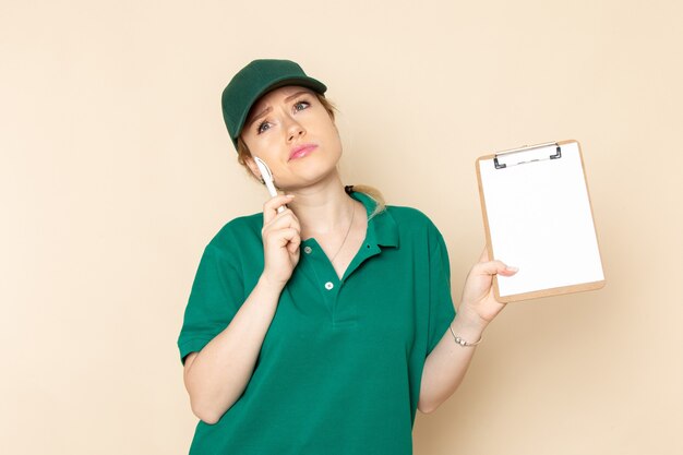 Vue de face jeune femme courrier en uniforme vert et cape verte tenant le bloc-notes en pensant à l'espace lumineux