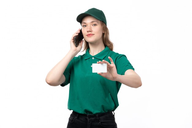 Une vue de face jeune femme courrier en uniforme vert parlant au téléphone et montrant une carte blanche