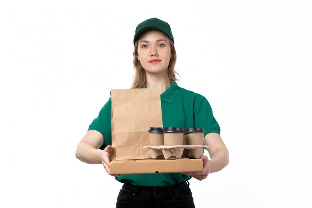 Une vue de face jeune femme courrier en uniforme vert souriant tenant des emballages alimentaires tasses à café
