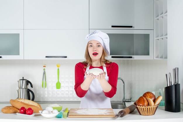 Vue de face jeune femme cuisinier en chapeau de cuisinier et tablier tenant la pâte