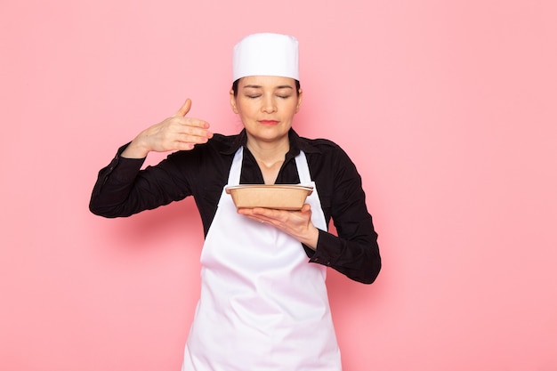 Une vue de face jeune femme cuisinier en chemise noire blanc cuisinier cape capuchon blanc posant l'odeur du lait brun bol
