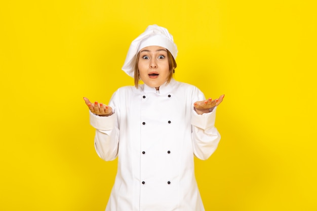 Une vue de face jeune femme cuisinier en costume de cuisinier blanc et chapeau blanc expression excitée sur le jaune