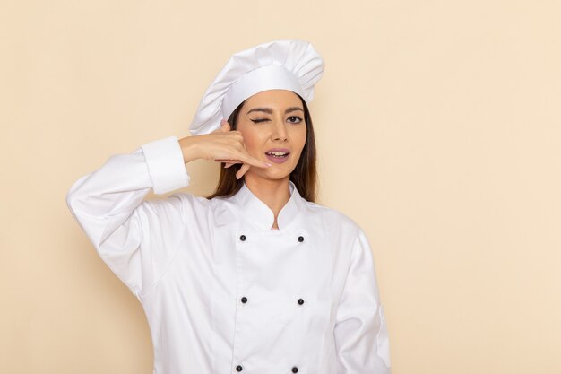 Vue de face de la jeune femme cuisinier en costume de cuisinier blanc clignotant sur un mur blanc clair