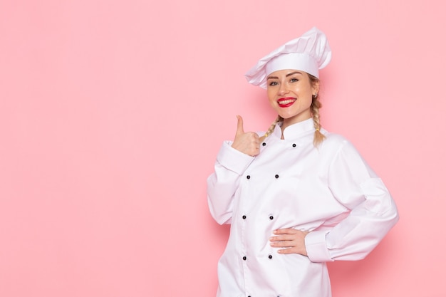 Vue de face jeune femme cuisinier en costume de cuisinier blanc posant avec une expression ravie sur la photo de cuisinier espace rose